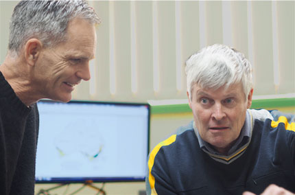 Two researchers having a conversation with office and computer screen showing crop model in background