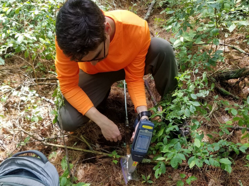 científico masculino arrodillado en el antiguo terreno de la huerta usando sonda de suelo y equipo